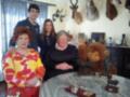Una familia de cuatro personas posa en una habitación con decoraciones de safari. La abuela, sentada en el centro, sostiene a un mono grande. A su lado, una mujer y un hombre sonríen junto a una niña en el fondo. La mesa tiene adornos de safari y un libro abierto.