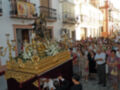 Una procesión religiosa con una estatua de oro y flores, acompañada por una multitud en un ambiente festivo.