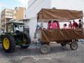 Una granja con un tractor verde y una carreta marrón, donde varias personas están sentadas.