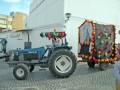 Un tractor azul con flores y un carrito adornado en una calle.