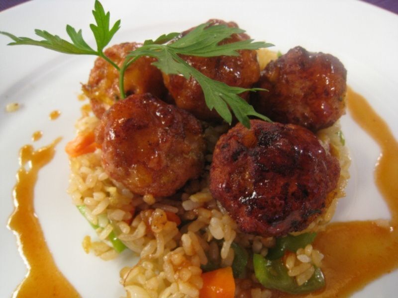 Un plato de arroz con verduras y albóndigas cubiertas de salsa de soja, adornado con hierbas frescas.
