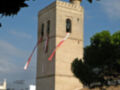 Torre de iglesia adornada con banderas rojas y blancas en un día soleado.