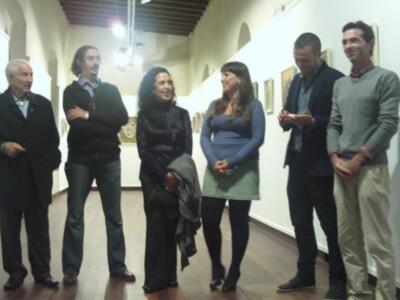 Una escena en una galería de arte, con varias personas observando y conversando sobre las obras expuestas en el fondo.