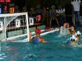 Juego de waterpolo femenino en acción, con jugadoras en el agua y un marcador que muestra los tiempos de juego.