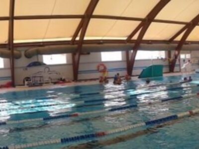 Piscina cubierta con techo de lona, líneas azules en el agua y paredes blancas.
