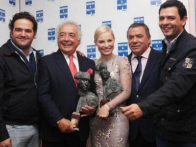 Una persona con un vestido de noche y una figura humana en su mano, rodeada por cuatro personas sonrientes.