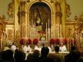 Celebración religiosa en un templo con sacerdotes y velas iluminando el altar.