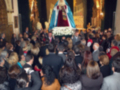 Una multitud en una iglesia, con personas vestidas de negro y ropa cálida. En el centro, una figura con un manto blanco y corona, rodeada de luces doradas. La imagen sugiere una ceremonia religiosa o funeral.