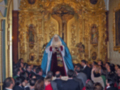 Una multitud congregada en un santuario, mirando hacia una imagen de San Pedro vestido con trajes dorados y azules. La decoración dorada del altar refleja la solemnidad de la celebración religiosa.