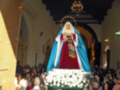Fotografía de una procesión religiosa en una iglesia, con una imagen venerada en el centro, rodeada de flores y una multitud de fieles observando la celebración.