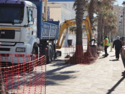 Camión con grúa amarilla, palmeras y trabajadores en la calle.