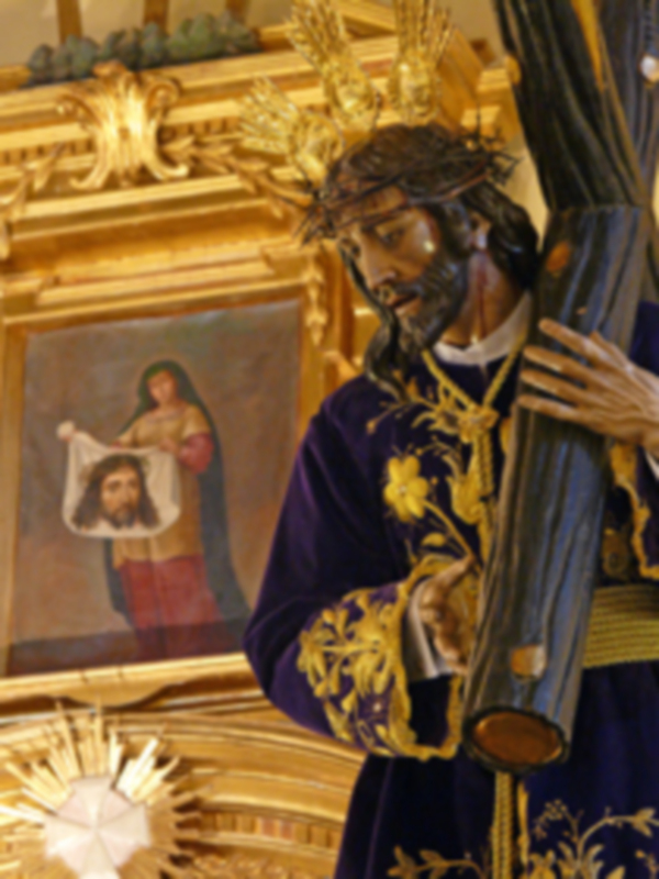 Retrato religioso de un santo con corona y vara, frente a una pintura que muestra a una figura humana.
