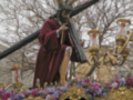 Una estatua de Jesús cargando la cruz, rodeada de flores y adornos dorados, en un entorno de árboles des有一天的天空。