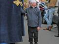 Un niño con un gorro de Papá Noel y una chaqueta azul se encuentra en el centro de la imagen, rodeado por otros individuos. La escena parece ser parte de una celebración navideña, posiblemente un desfile o evento familiar.