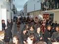Una procesión religiosa con personas vestidas de manera tradicional, llevando banderas y tocados.