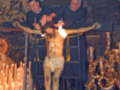 Imagen de un crucificado en la iglesia, con velas encendidas y una persona rezando.