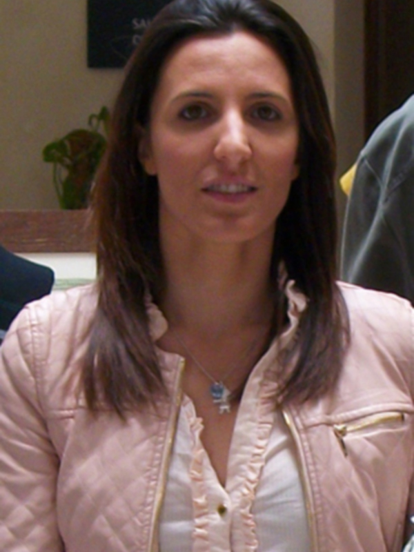 Una mujer con cabello largo y ondulado, vistiendo una chaqueta rosa y una camisa blanca, posando para la cámara.
