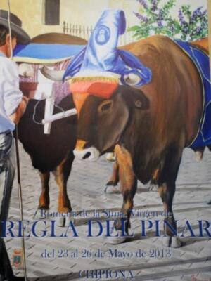 Una imagen de un toro con una capa azul y amarilla, posiblemente en una fiesta o celebración. La fecha menciona la Romería de la Sina, Viguera de Regla del Pinar en Chipion.