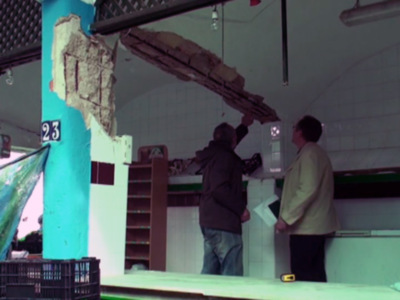 Dos personas trabajando en la reparación de un techo, con una pared azul y una puerta abierta en el fondo.