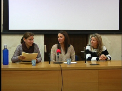 Tres mujeres sentadas en una mesa con un micrófono y documentos, probablemente en una conferencia o reunión.