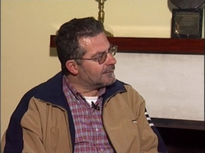 Hombre con gafas y chaqueta marrón hablando en una entrevista o conversación formal.