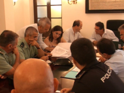 Una reunión de trabajo en una sala con mesas y sillas, donde varias personas están sentadas y discutiendo. La imagen muestra a varios individuos, algunos de ellos con uniformes policiales, en un ambiente formal. La escena transmite una atmósfera de colaboración y discusión.
