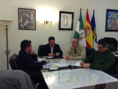 Tres personas discuten en una sala de reuniones con una bandera española y un mapa en el escritorio.