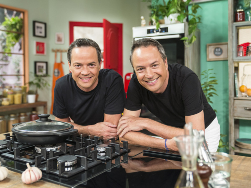 Dos hombres sonrientes en una cocina moderna, frente a un horno y estufa. La imagen muestra detalles de la decoración y los utensilios de cocina, enfocándose en un ambiente acogedor y bien organizado.