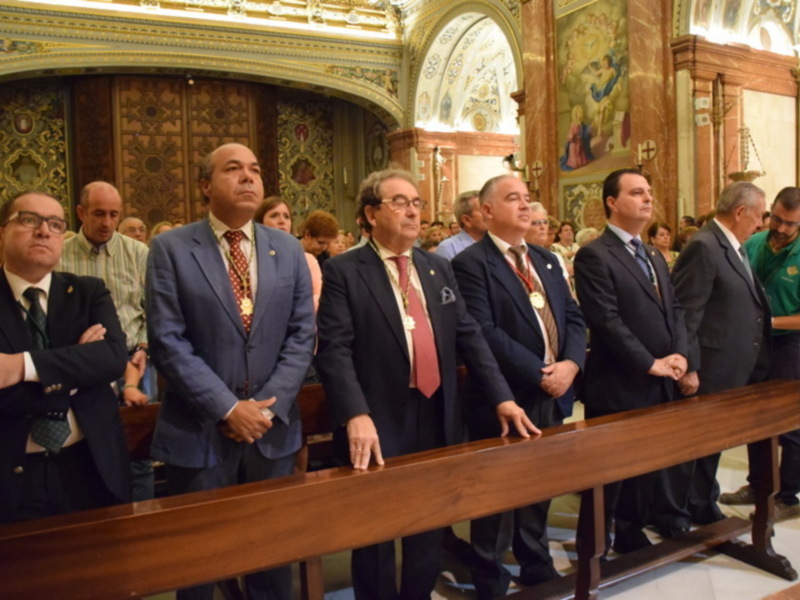 Un grupo de hombres vestidos con trajes formales se encuentran en una sala ricamente decorada, posiblemente dentro de un edificio histórico o ceremonial. La atmósfera es formal y solemnemente decorada con mosaicos y adornos dorados.
