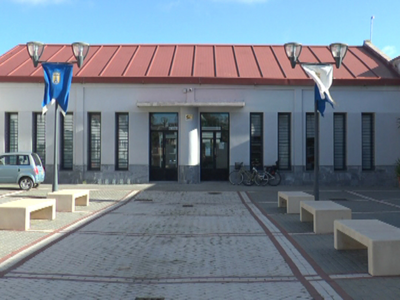 Edificio público con techo rojo y ventanas blancas, banderas ondeando en el exterior.