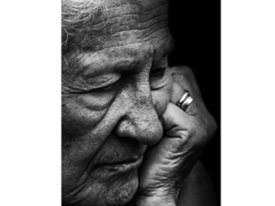 Una imagen en blanco y negro de una persona mayor con la mano levantada a su mejilla, expresando tristeza o dolor.