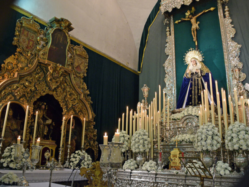Altar con imágenes religiosas, velas y flores, decorado con oro y plata.