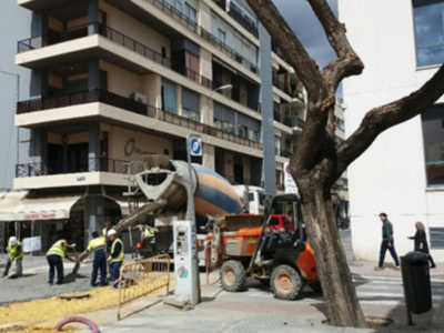 Trabajadores en una obra de construcción, con un camión hormigonera y una árbol en el camino.