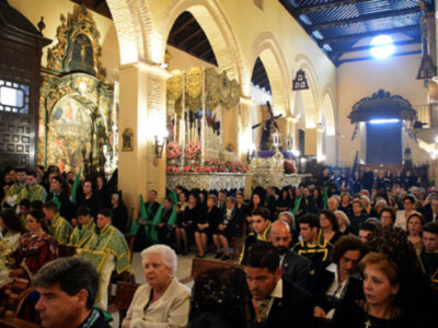 Una multitud de personas en una iglesia con vestimentas coloridas, posiblemente durante una celebración religiosa. La arquitectura es de estilo barroco, con altas cúpulas y detalles dorados. La iluminación es natural, proveniente de ventanas altas en la parte superior del edificio.