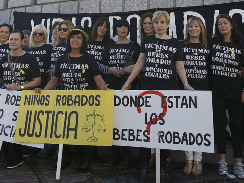Grupos de personas con camisetas que dicen 'Víctimas de bebés robados y adopciones ilegales' sostienen pancartas que reclaman justicia para las víctimas de la adopción ilegal.