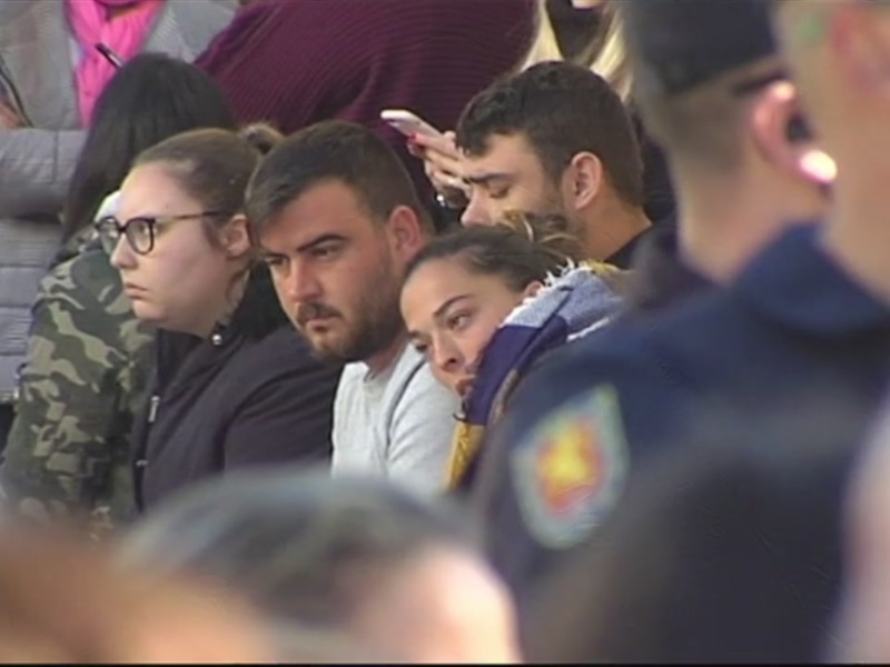 Un grupo de personas, algunas con chaquetas y gorras, observan algo atentamente. La imagen parece ser de una transmisión televisiva o un evento público.