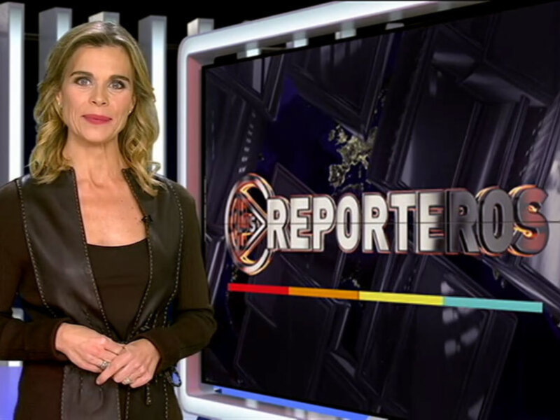 Reportera en un set de noticiero con el logo de la cadena en el fondo.