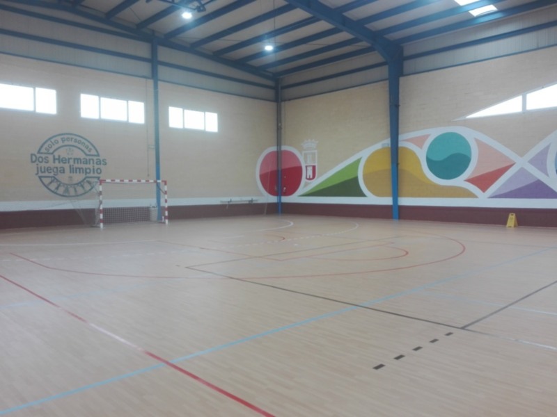 Interior de una cancha deportiva con marcaciones para fútbol sala y baloncesto, mural decorativo y puerta de portería.