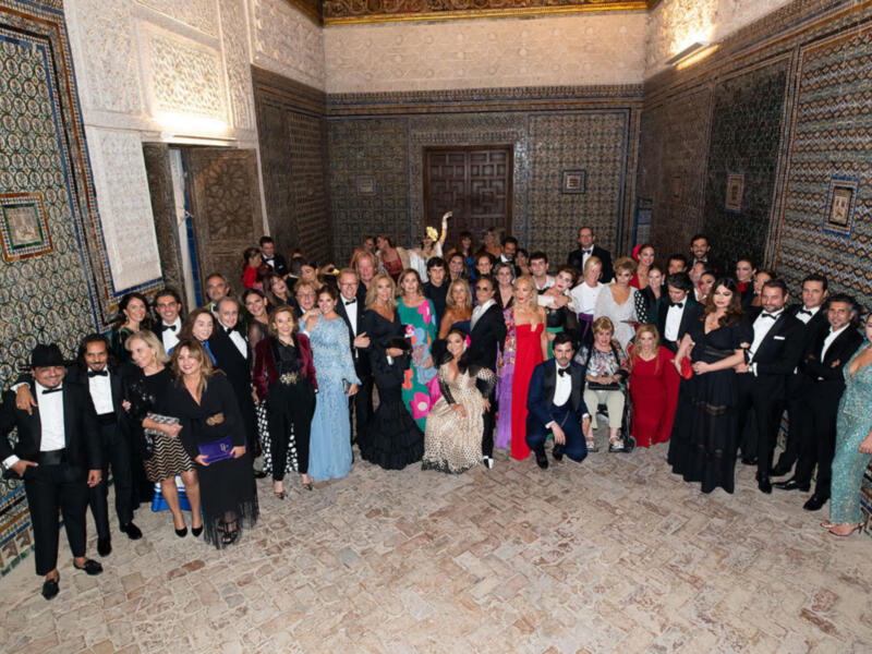 Una multitud de personas posa en un salón decorado con mosaicos y azulejos, todos vestidos formalmente. La imagen muestra una celebración o evento importante en un ambiente histórico y elegante.