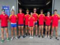 Equipo de atletas en uniforme rojo y azul, posando frente a una puerta de gimnasio.