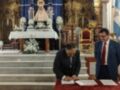 Dos personas firman documentos en una iglesia con un altar y flores.