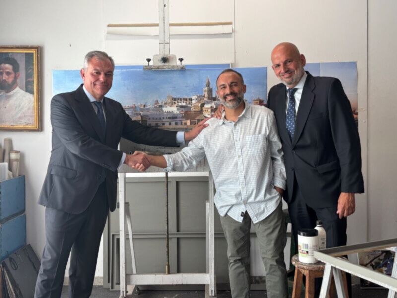 Tres hombres en trajes de negocios están apretando las manos, con una pintura de un paisaje en el fondo. La escena sugiere una reunión formal o un acuerdo entre los individuos.