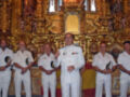 Un grupo de hombres en uniforme militar, posiblemente oficiales, se encuentran en una sala de mosaicos y estatuas religiosas. El ambiente es formal, con un altar dorado en el fondo y una bandera española visible.