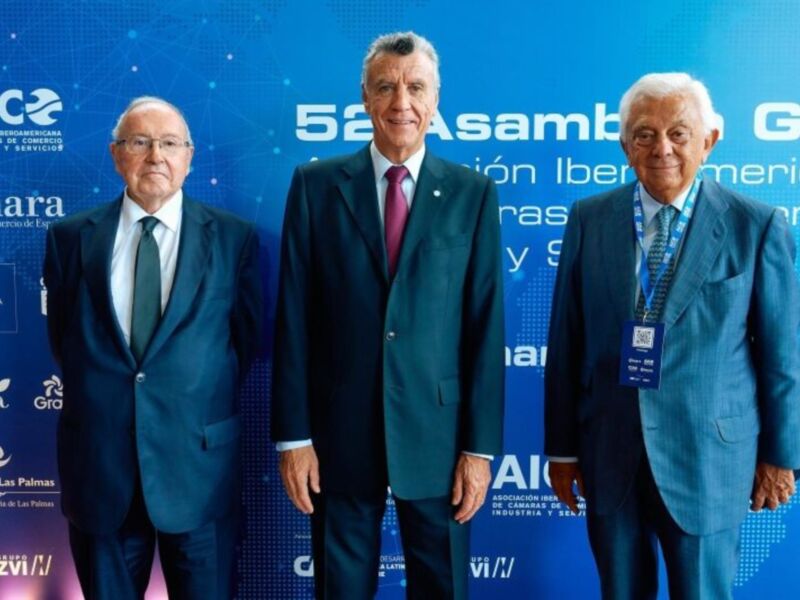 En la 52 Asamblea General de la AICE, tres hombres en trajes formales posan frente a un fondo azul con el logo de la asociación.