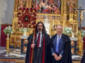 Dos hombres vestidos con trajes ceremoniales posan frente a un altar dorado y una imagen religiosa.