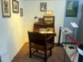 Una antigua mesa de escritorio con una silla de madera, en un museo. La pared está decorada con fotos y un cartel informativo sobre una persona importante.