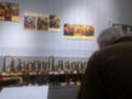 Un hombre examina una colección de estatuillas doradas en un escaparate, con carteles históricos colgados en la pared de fondo.