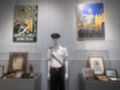En el museo, una figura de uniforme se encuentra en un vitrina junto a otros objetos históricos. La pared al fondo muestra una imagen de un edificio antiguo y otro cartel con información sobre el aniversario 2006-2036.